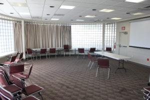 Carpeted room with stacked chairs, table and windows.